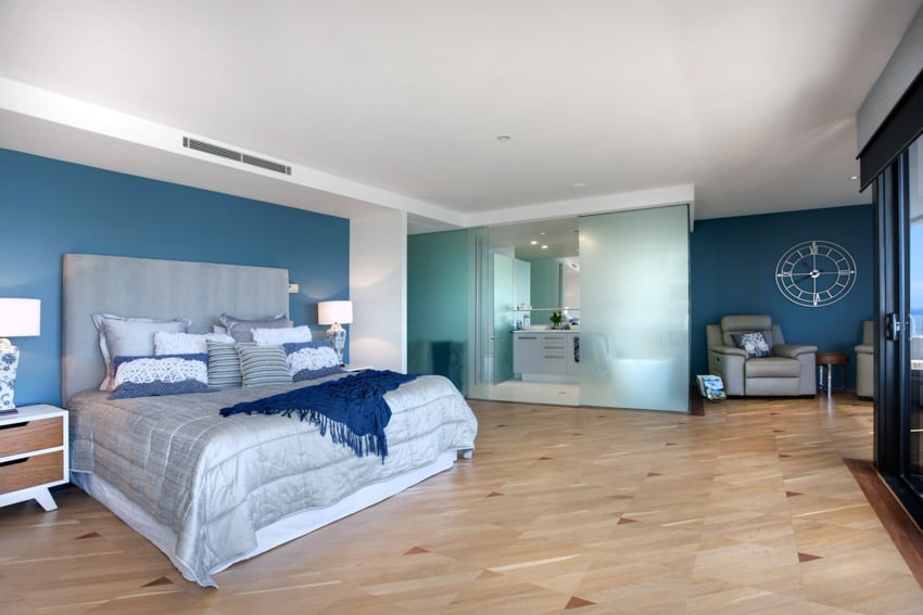 Bedroom with blue accent wall, comforter, headboard, pillows, nightstands, lamps, and wood flooring