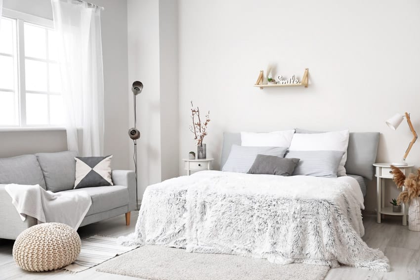 Bedroom with sofa, bedding, pouf, pillows, lamp, nightstand, floating shelf, and window curtains