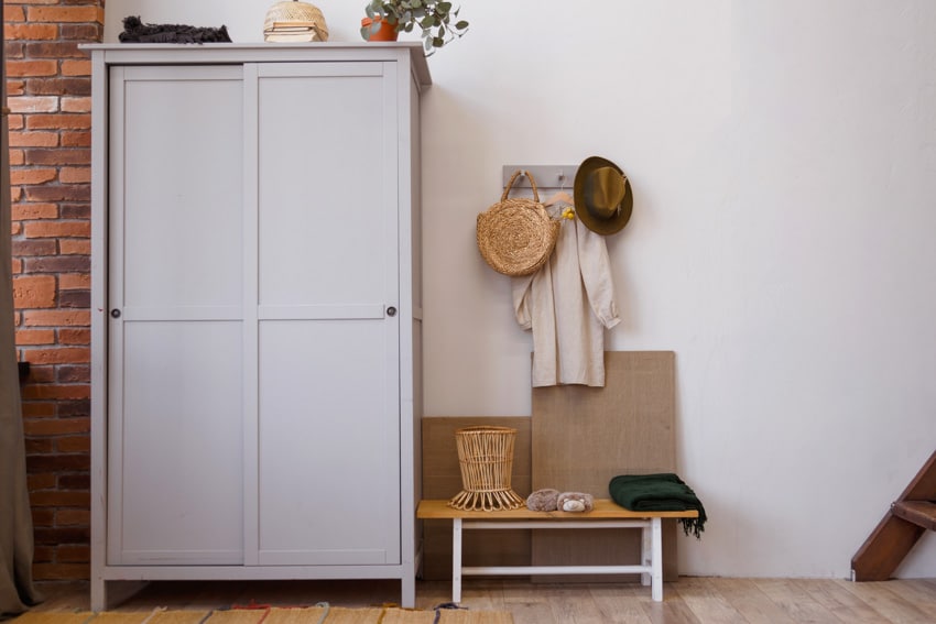 Gray closet armoire, small bench, and brick accent wall