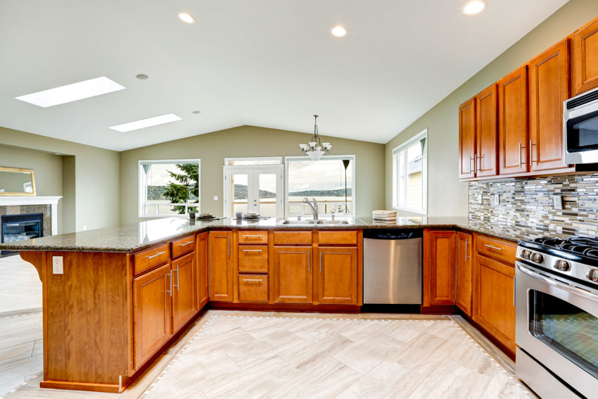 Kitchen with wood cabinets, sage toned wall, backsplash, oven, stove, windows, and ceiling lights
